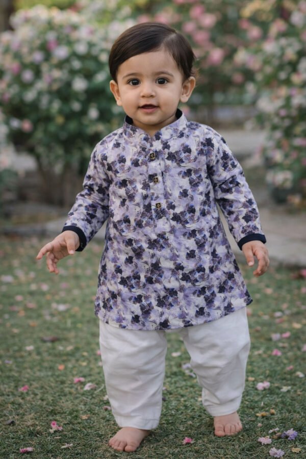 Baby boy wearing grey and blue abstract print kurta and white pajama, outdoor garden setting.